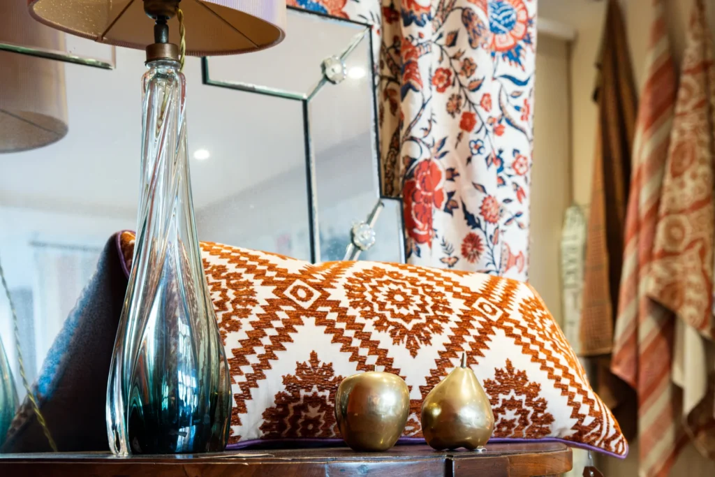Glazen lampvoet, kussen met oranje motief en gouden peren voor gordijnstoffen bij Pomegranate aan de Van Hoytemastraat in Den Haag