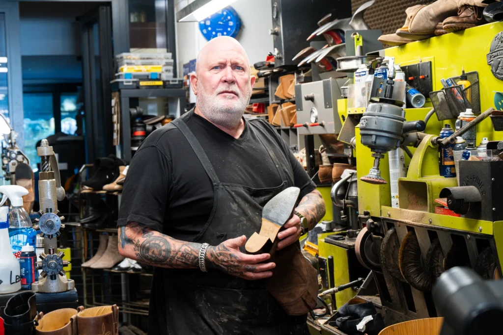 Schoenmaker met een schoen in de hand in de werkplaats bij Schoenmakerij Lauwers aan de Van Hoytemastraat in Den Haag